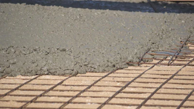 Wet concrete being poured over metal reinforcement mesh during construction flooring work