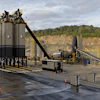 Industrial concrete batch plant with tall storage silos and conveyor systems at an active quarry site