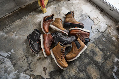 Collection of brown and black work boots and casual lace-up boots displayed on weathered concrete ground