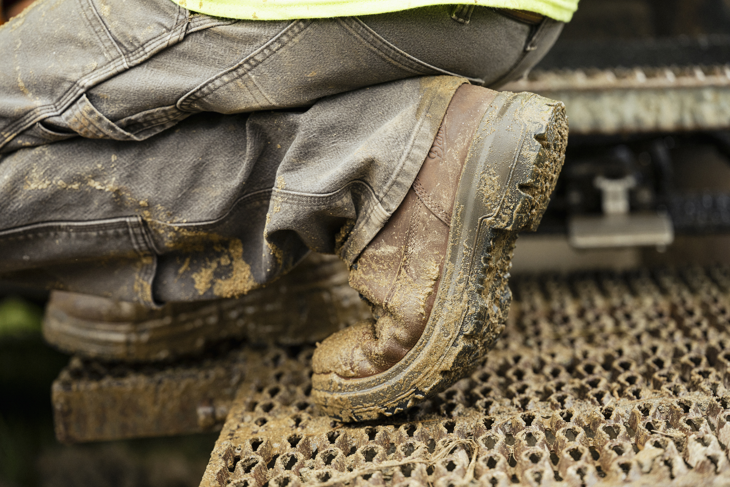 Worker in mud-caked boots and jeans standing on industrial textured surface