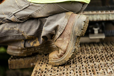 Worker in mud-caked boots and jeans standing on industrial textured surface