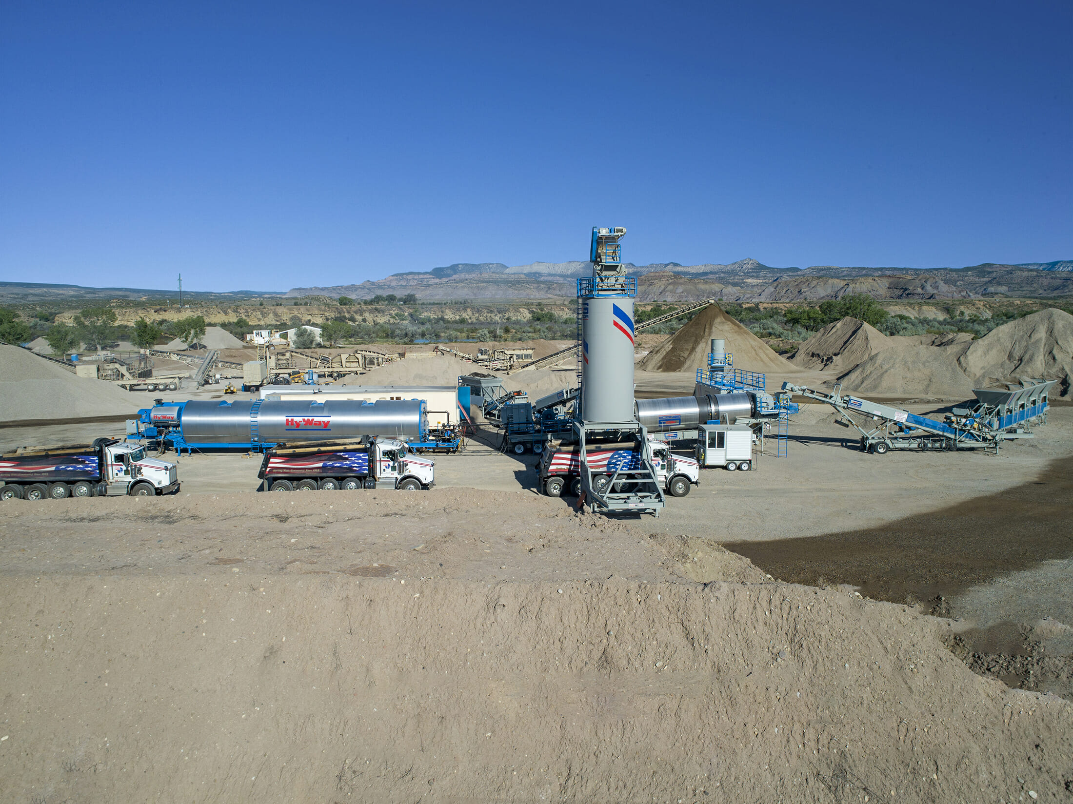 Industrial concrete batching plant with trucks, storage tanks, and aggregate piles in desert landscape
