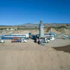Industrial concrete batching plant with trucks, storage tanks, and aggregate piles in desert landscape