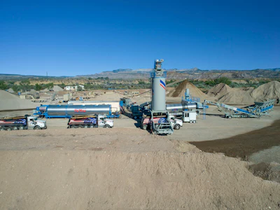 Industrial concrete batching plant with trucks, storage tanks, and aggregate piles in desert landscape