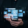 Person holding smartphone displaying floating digital interface icons including user profile, analytics charts, and communication symbols