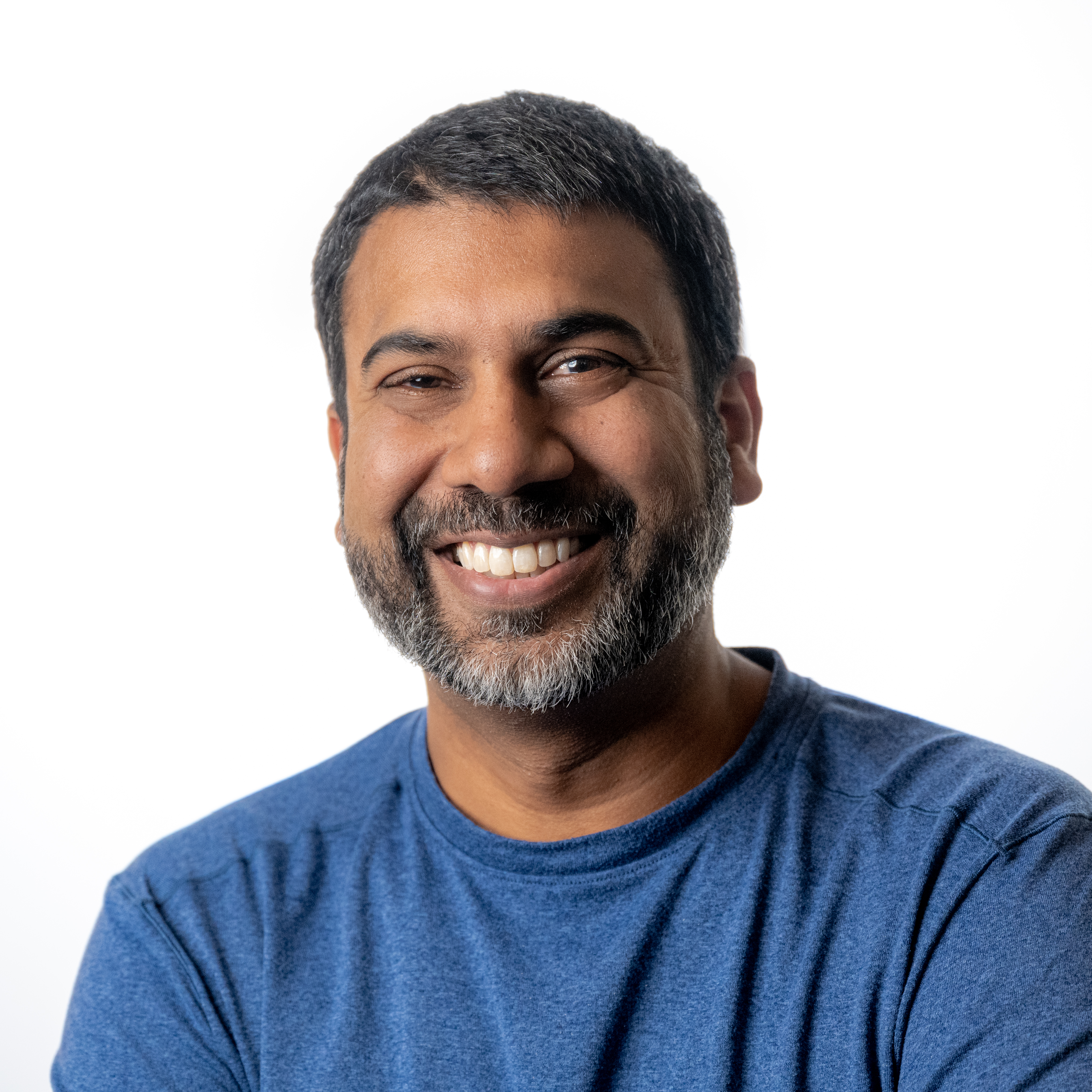 Smiling man with dark beard wearing blue t-shirt against white background Headshot