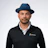 Professional man wearing blue fedora and black Planera-branded jacket over white shirt Headshot