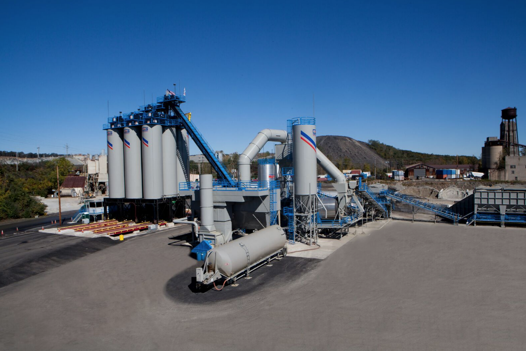 Industrial concrete batch plant with large storage silos, blue conveyor systems, and processing equipment on a paved facility