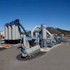 Industrial concrete batch plant with large storage silos, blue conveyor systems, and processing equipment on a paved facility