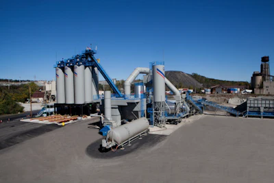 Industrial concrete batch plant with large storage silos, blue conveyor systems, and processing equipment on a paved facility
