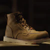 Tan leather work boots with white soles displayed on dark surface with dramatic lighting