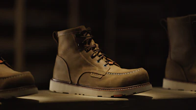 Tan leather work boots with white soles displayed on dark surface with dramatic lighting