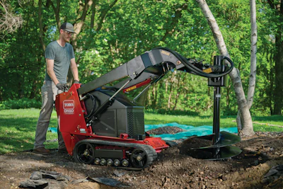 Man operating red Toro DFS540 compact tracked loader with auger attachment in wooded yard setting