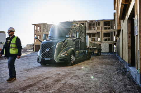 Construction worker in safety gear observing a blue Volvo semi-truck at an active building site