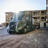 Construction worker in safety gear observing a blue Volvo semi-truck at an active building site