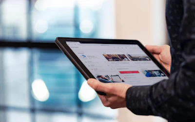 Person holding tablet displaying website with content cards and navigation interface in modern office setting