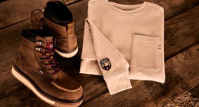 Brown leather work boots with cream crew neck sweater and watch arranged on wooden surface