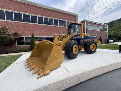 Yellow and blue wheel loader with bucket attachment parked in front of brick industrial building