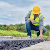 Construction worker in safety gear inspecting asphalt pavement on a road project
