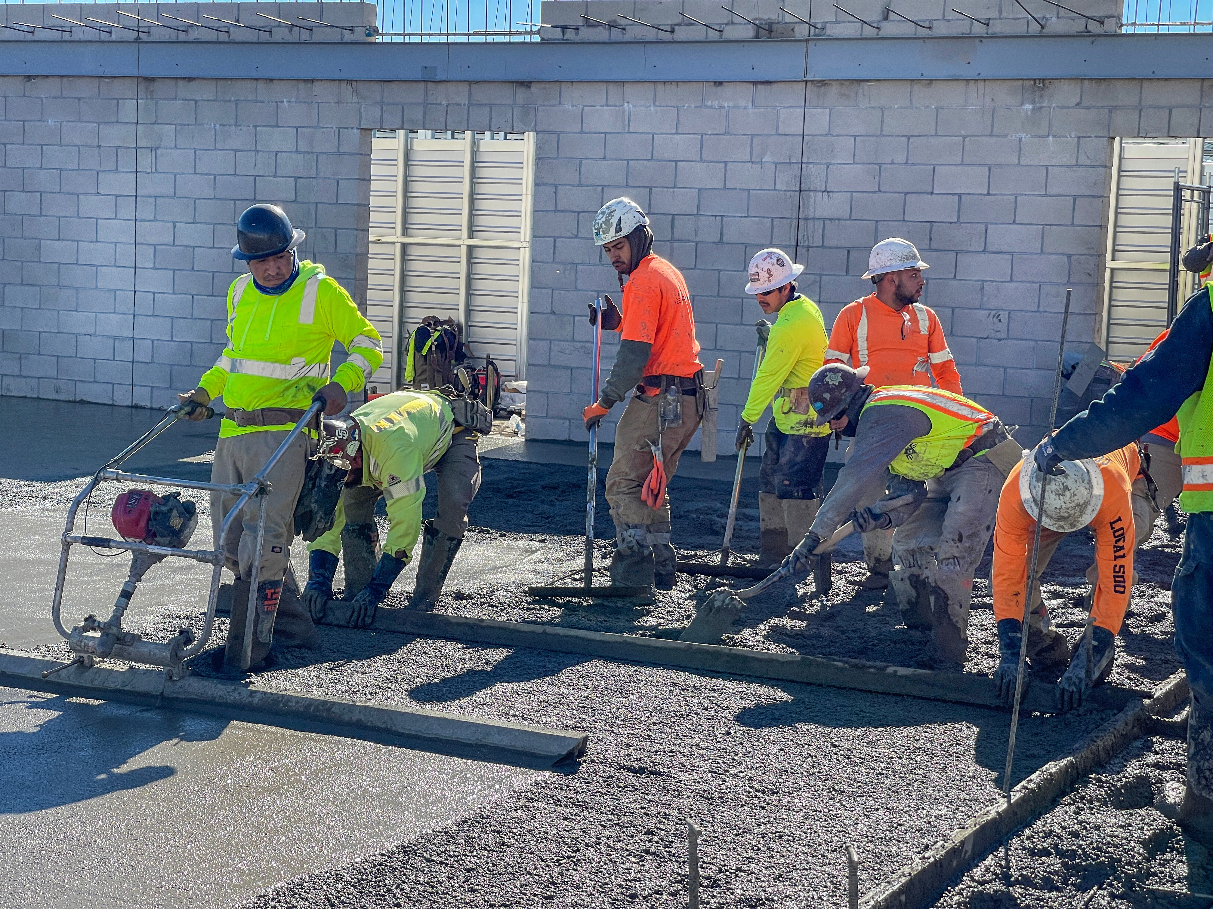 Construction workers in safety gear operating concrete finishing equipment on a job site