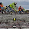 Construction workers in safety gear pouring concrete on a building site with yellow marking visible