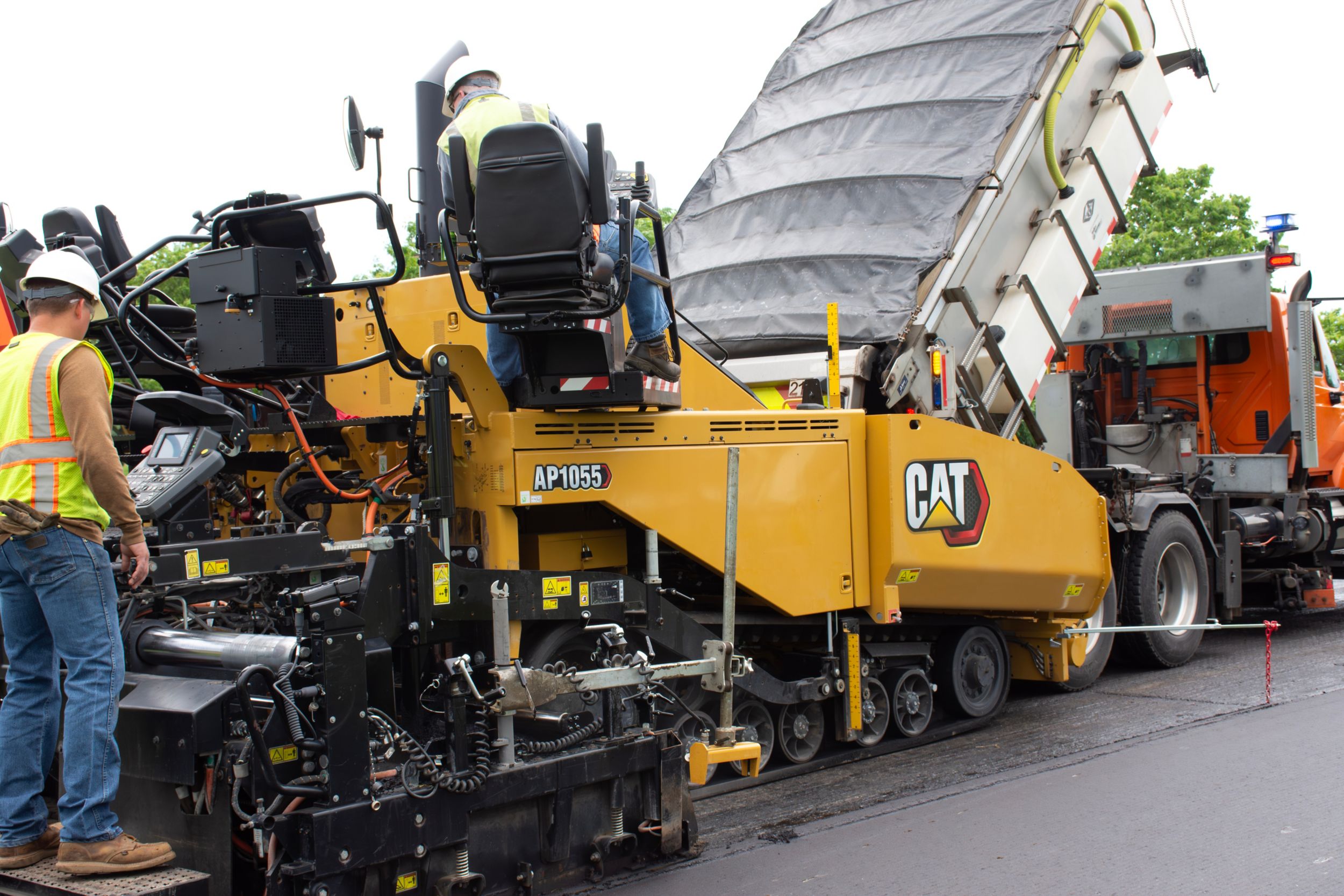 Yellow Caterpillar asphalt paver and dump truck at construction site with workers in safety gear