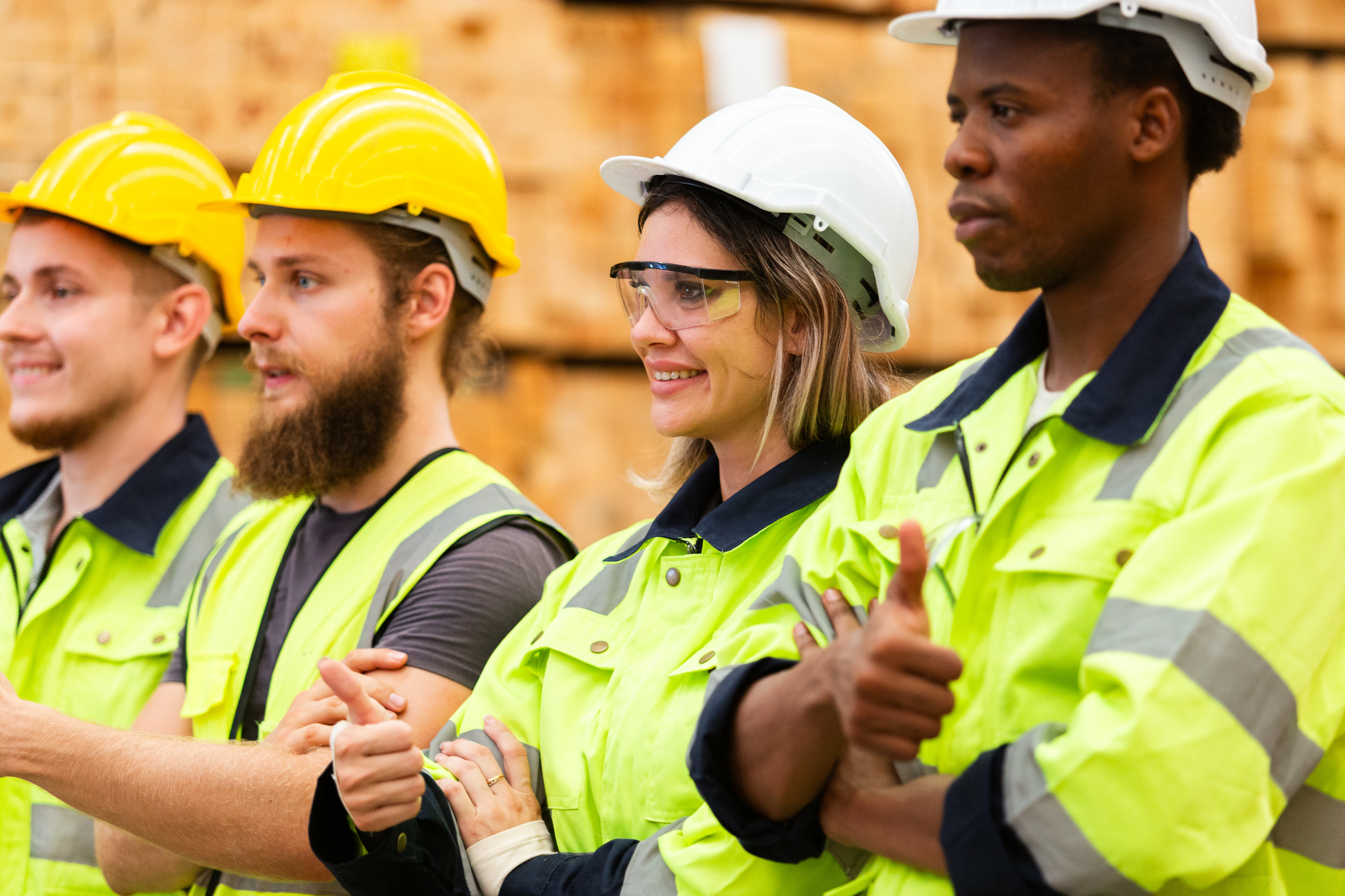 Four construction workers in safety helmets and high-visibility vests standing together at a job site