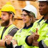 Four construction workers in safety helmets and high-visibility vests standing together at a job site
