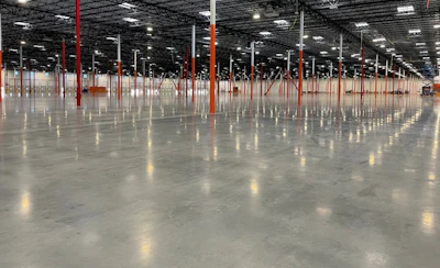 Empty industrial warehouse interior with red support columns, polished concrete floor, and overhead LED lighting