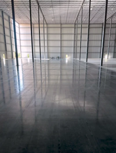 Empty industrial warehouse interior with metal framework, polished concrete floor, and structural support columns
