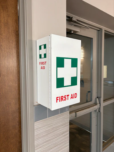 White first aid cabinet with green cross symbol mounted on wall near glass door