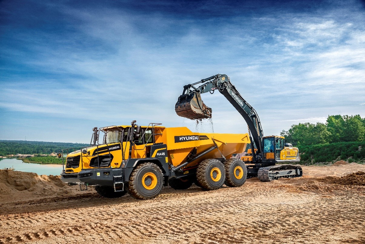 Yellow Hyundai wheel loader and excavator operating at a gravel quarry site with water and trees in background