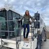 Woman posing on Wirtgen industrial truck with tire racks and bare landscape in background