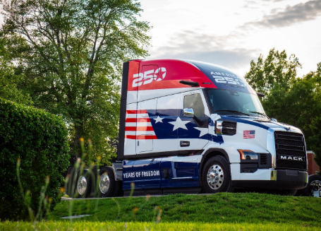 Mack truck with patriotic Heart of Freedom livery featuring American flag design on cab, parked in grassy field with trees