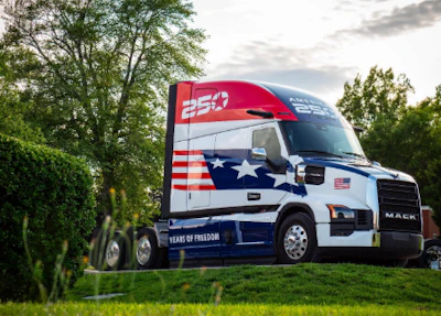 Mack truck with patriotic Heart of Freedom livery featuring American flag design on cab, parked in grassy field with trees