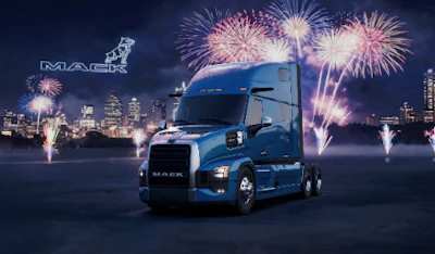 Blue Mack semi-truck displayed against illuminated city skyline with celebratory fireworks bursting overhead at night