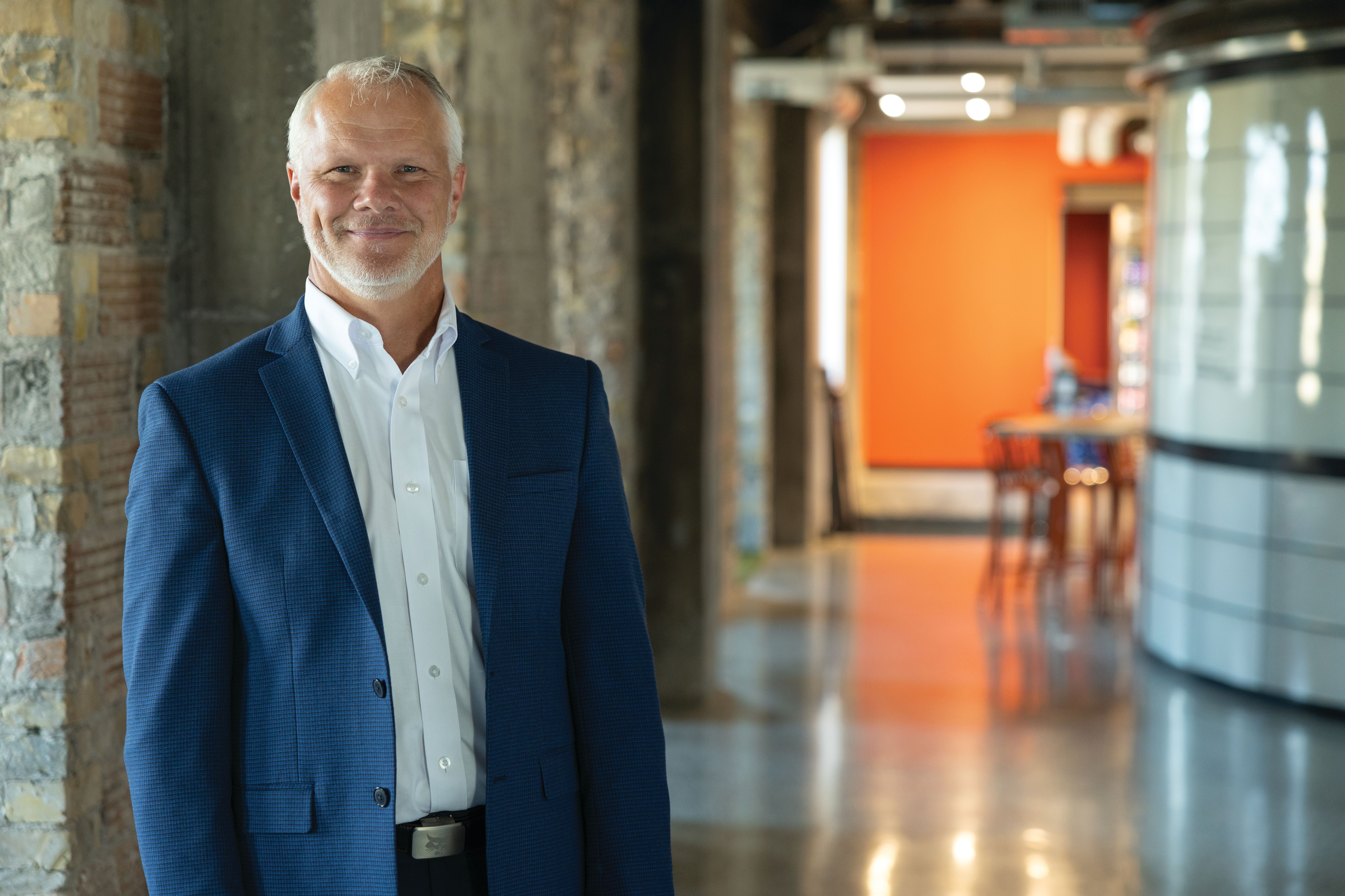 Professional businessman in blue blazer standing in modern office corridor with orange accent wall
