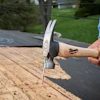 Milwaukee claw hammer with wooden handle being used on roof shingles during construction work
