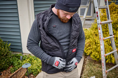 Worker wearing black Milwaukee branded vest and gloves standing near ladder and garden plants