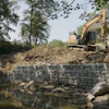 Construction site with yellow excavator building retaining wall beside residential home