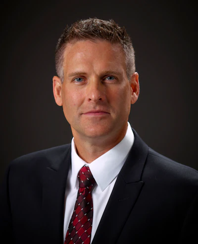 Professional headshot of a man in dark suit and burgundy tie against dark background