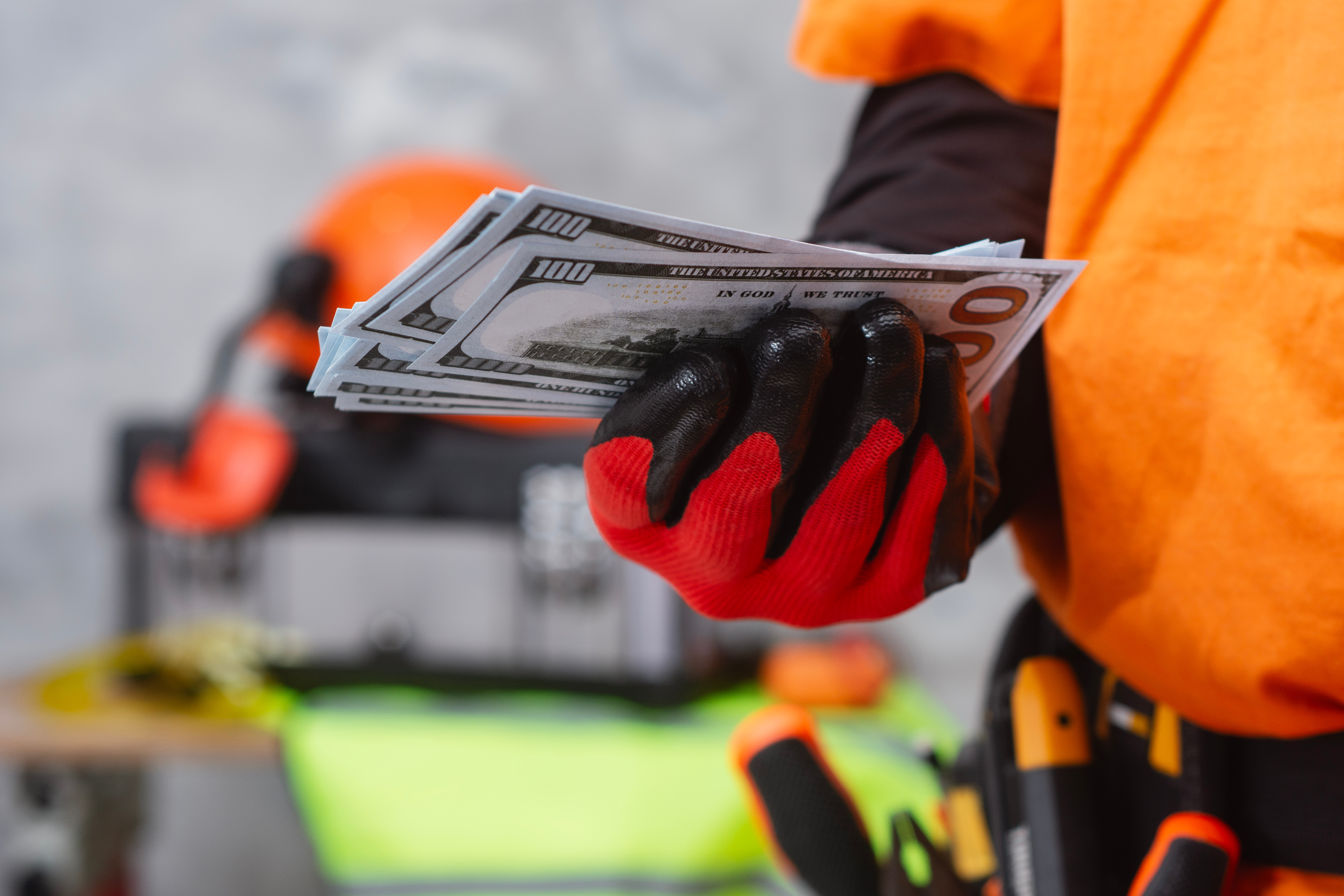 Person in orange winter jacket holding Euro banknotes with red and black gloves outdoors