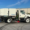 White Schwarze street sweeper truck with blue and black mechanical broom equipment parked on asphalt near industrial buildings