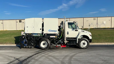 White Schwarze street sweeper truck with blue and black mechanical broom equipment parked on asphalt near industrial buildings