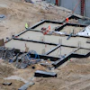 Aerial view of construction site foundation with concrete forms, rebar, and workers in safety equipment