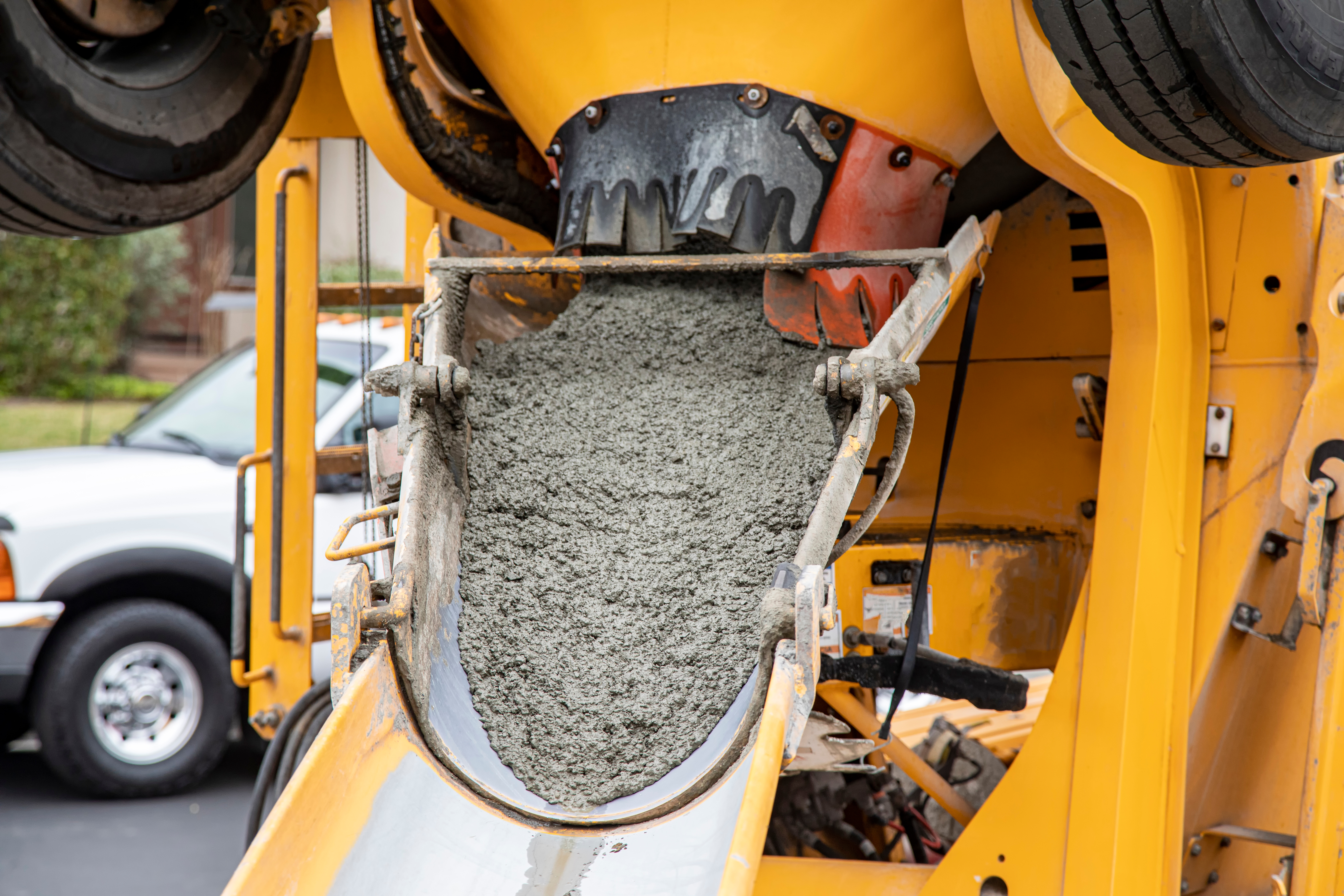 Yellow concrete mixer truck with rotating drum filled with wet gray concrete at job site