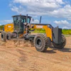 Yellow CASE motor grader operating on dirt road with green landscape and blue sky