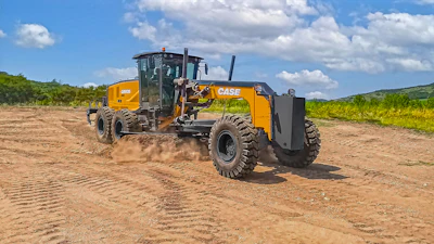 Yellow CASE motor grader operating on dirt road with green landscape and blue sky