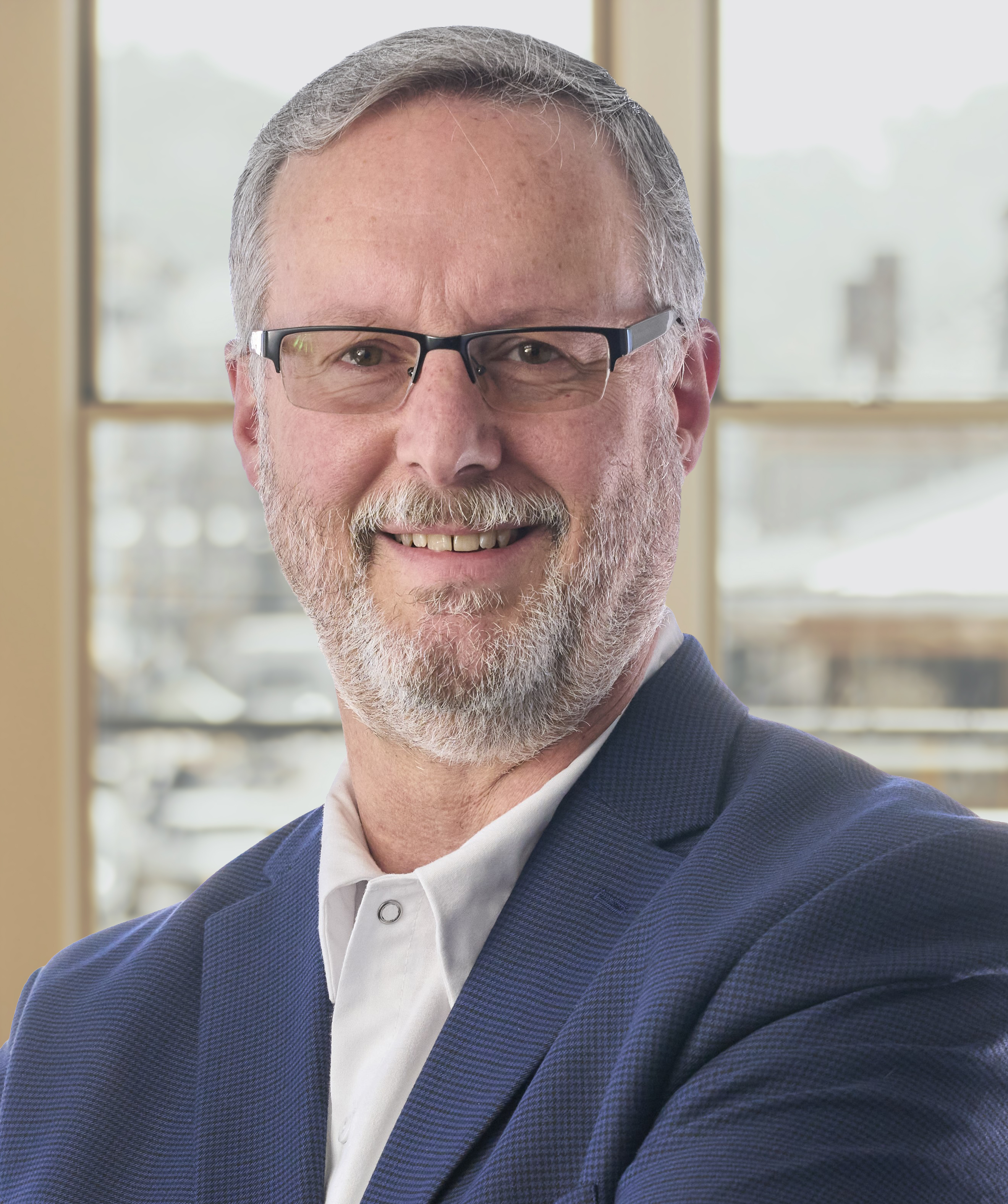 Professional headshot of a bearded man wearing glasses and navy blazer in modern office setting