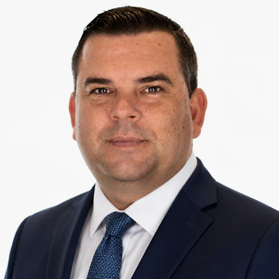Professional headshot of a man in dark business suit and blue tie against white background